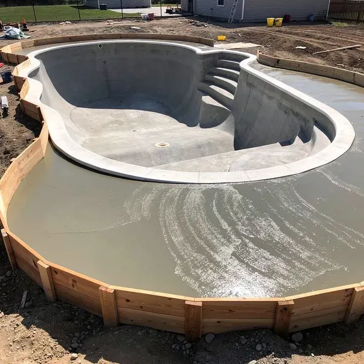 Concrete pool deck under construction around a new empty pool shell in Ashland, Oregon