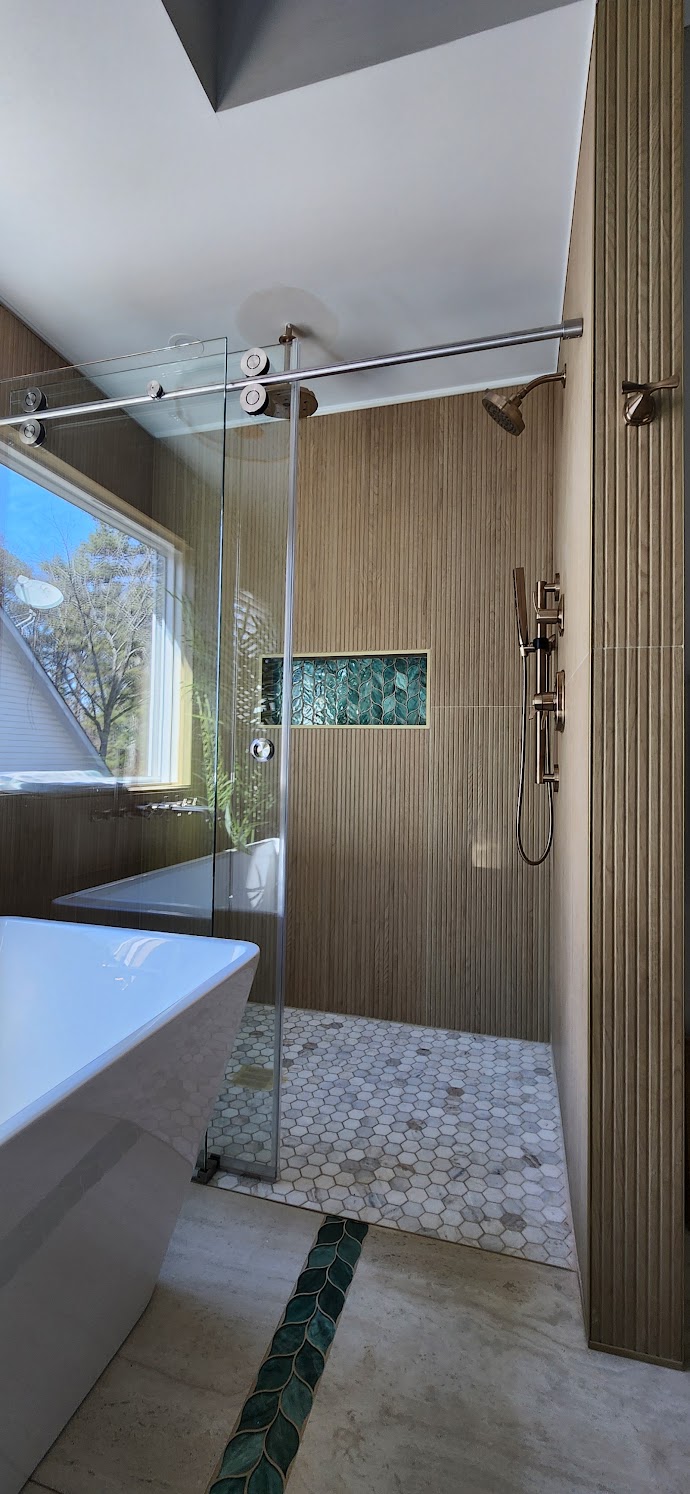 Finished wood panel shower with green marble niche, pebble floor and freestanding tub