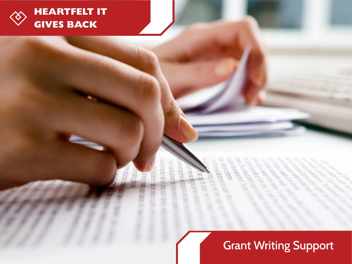 close-up photograph of hands with a pen reviewing complex grant documents on a desk, with specified "Grant Writing Support" and Heartfelt IT Gives Back branding overlays.