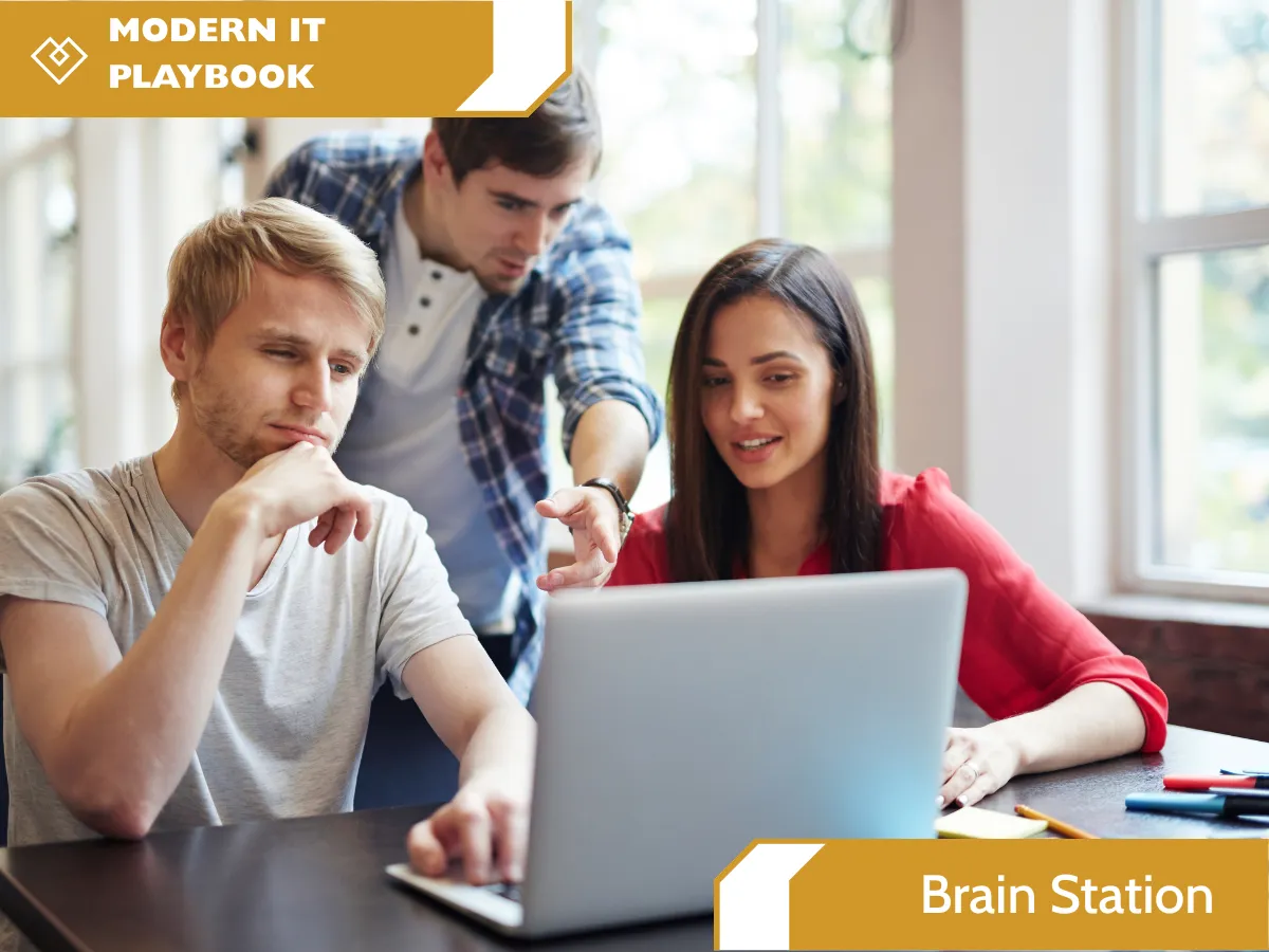 Three colleagues collaborating around a laptop computer in a bright office environment. A yellow banner in the top-left corner reads "MODERN IT PLAYBOOK" and another yellow banner in the bottom-right corner reads "Brain Station".