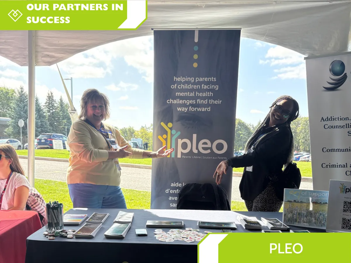Community outreach booth by Parents’ Lifeline (PLEO) at outdoor event, promoting mental health support for parents of children facing challenges, with brochures, banners, and smiling volunteers