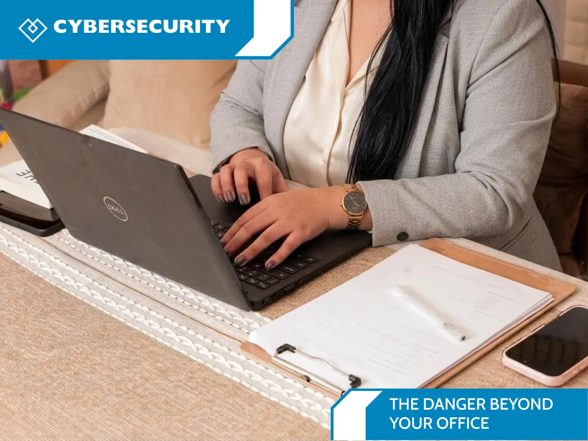 Remote worker using a laptop at a table with a phone and paperwork nearby.