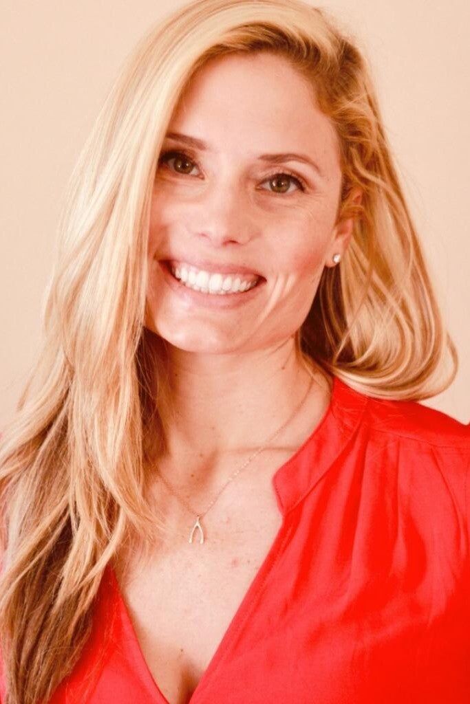 Portrait of Brittney, founder of Onedery, smiling confidently in a vibrant office, wearing a bold blue blazer, with creative marketing materials in the background. The image radiates approachability and leadership.