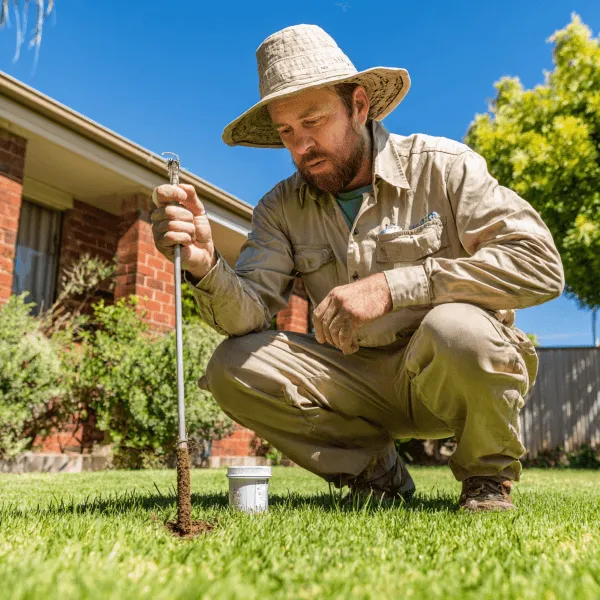 A lawn care worker doing a soil test in gras he is hlding a sil testing device