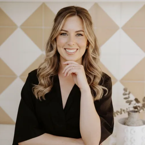 Portrait of the founder: a confident mid-30s female with warm expression, standing in a softly lit studio against a neutral background, waist-up composition, natural tones to convey trust and approachability.