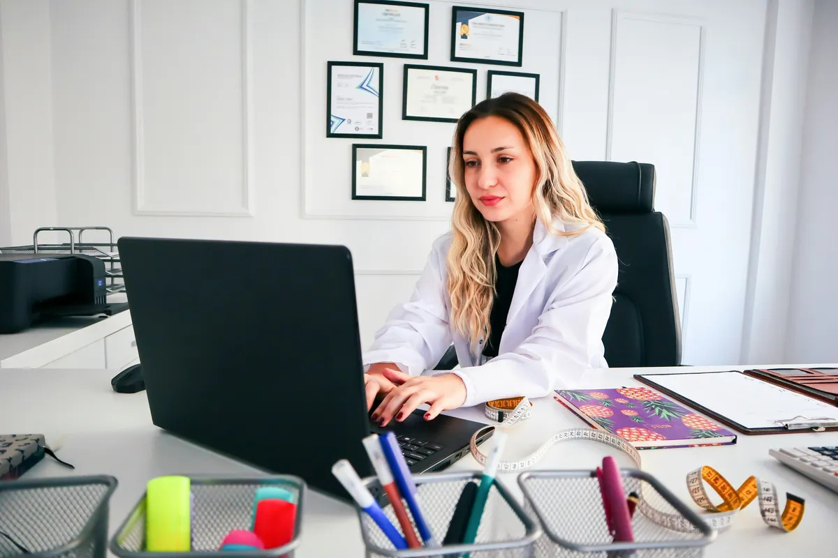 Physician or practice manager reviewing software on a laptop or tablet in a clean, modern medical office setting. Warm, professional atmosphere.