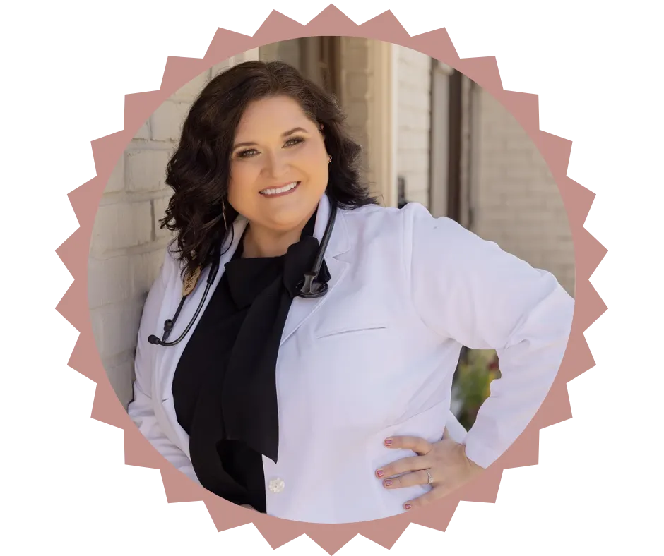 Portrait of Charlsie Gillcoat, NP, founder of The903NP, a private medical practice. She is smiling confidently, wearing a white coat with a stethoscope around her neck, standing against a light brick wall with her hand on her hip.