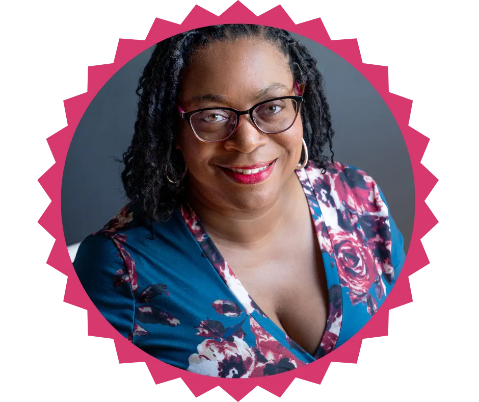  Portrait of Dr. Denise Dennis, CEO of ActionAccelerated, smiling warmly. She is wearing glasses, a floral-patterned blue dress, and hoop earrings, with a dark background highlighting her confident and approachable demeanor.