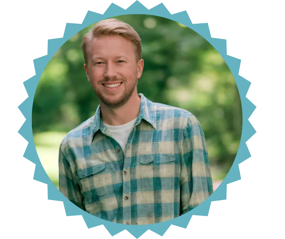  Portrait of Tristan Clements, founder of Answers By Fire Ministries, smiling outdoors. He is wearing a blue and white plaid shirt with a white undershirt, standing in front of a blurred natural background.