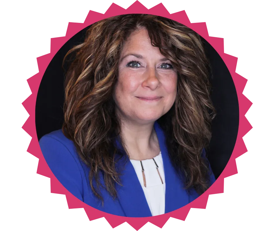 Portrait of Tobie Knaub, CEO of TMK Consulting, smiling confidently. She has wavy brown hair with highlights and is wearing a royal blue blazer and a white blouse, set against a dark background.