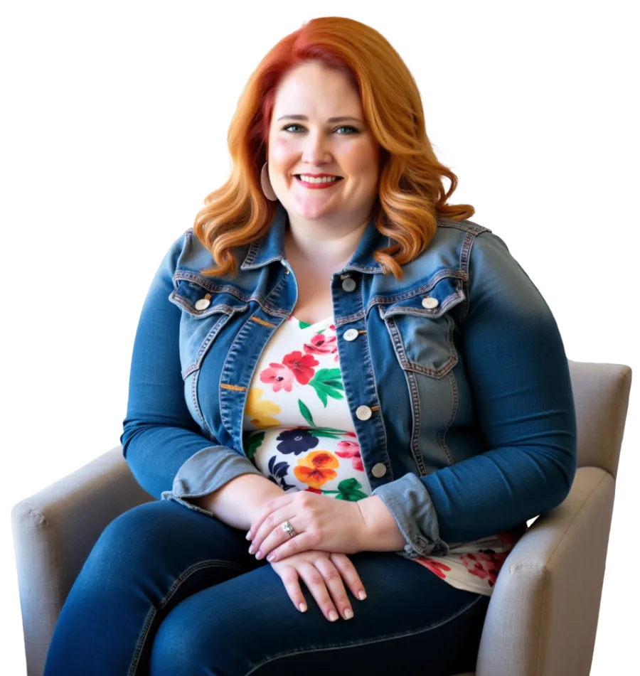 Caitlin, a red-haired professional, is seated confidently in a light beige chair. She’s wearing a denim jacket over a floral top, paired with jeans. Caitlin smiles warmly, radiating approachability and professionalism, ready to connect and strategize.