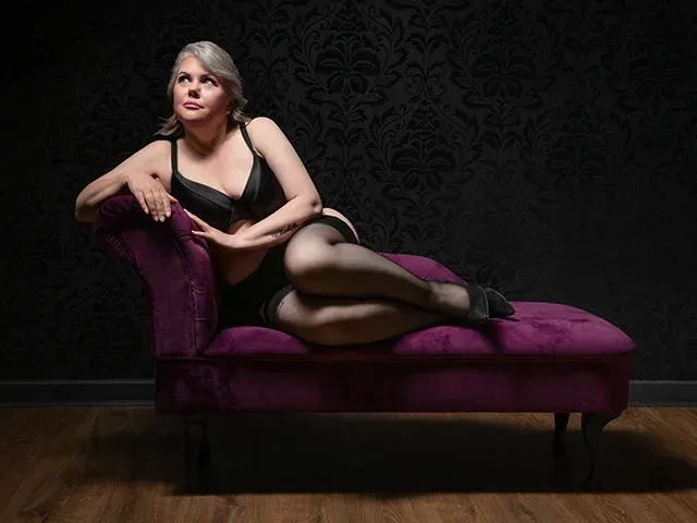 Woman in black lingerie sitting on a chaise.