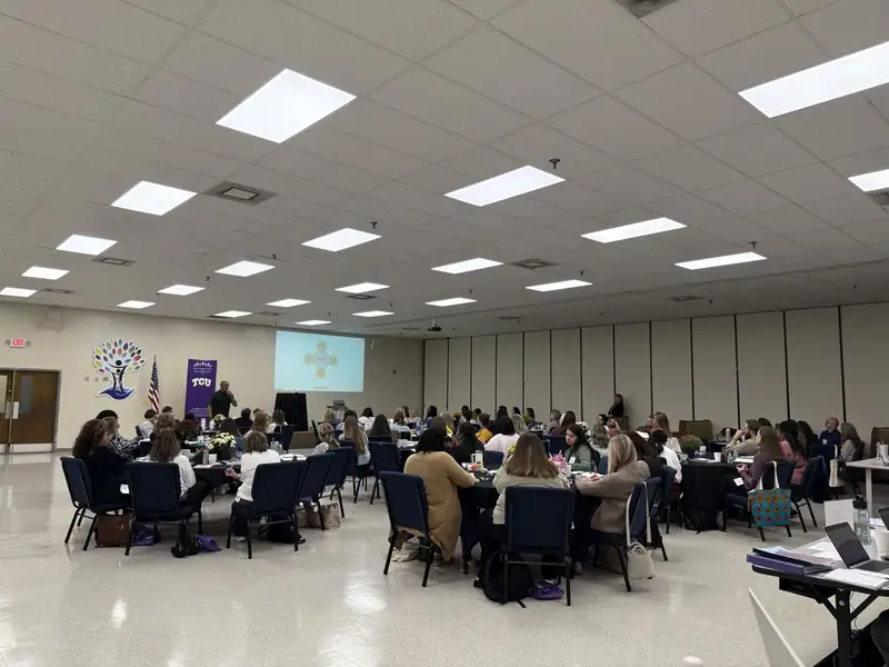 Classroom setting with attendees seated at round tables listening to an instructor.