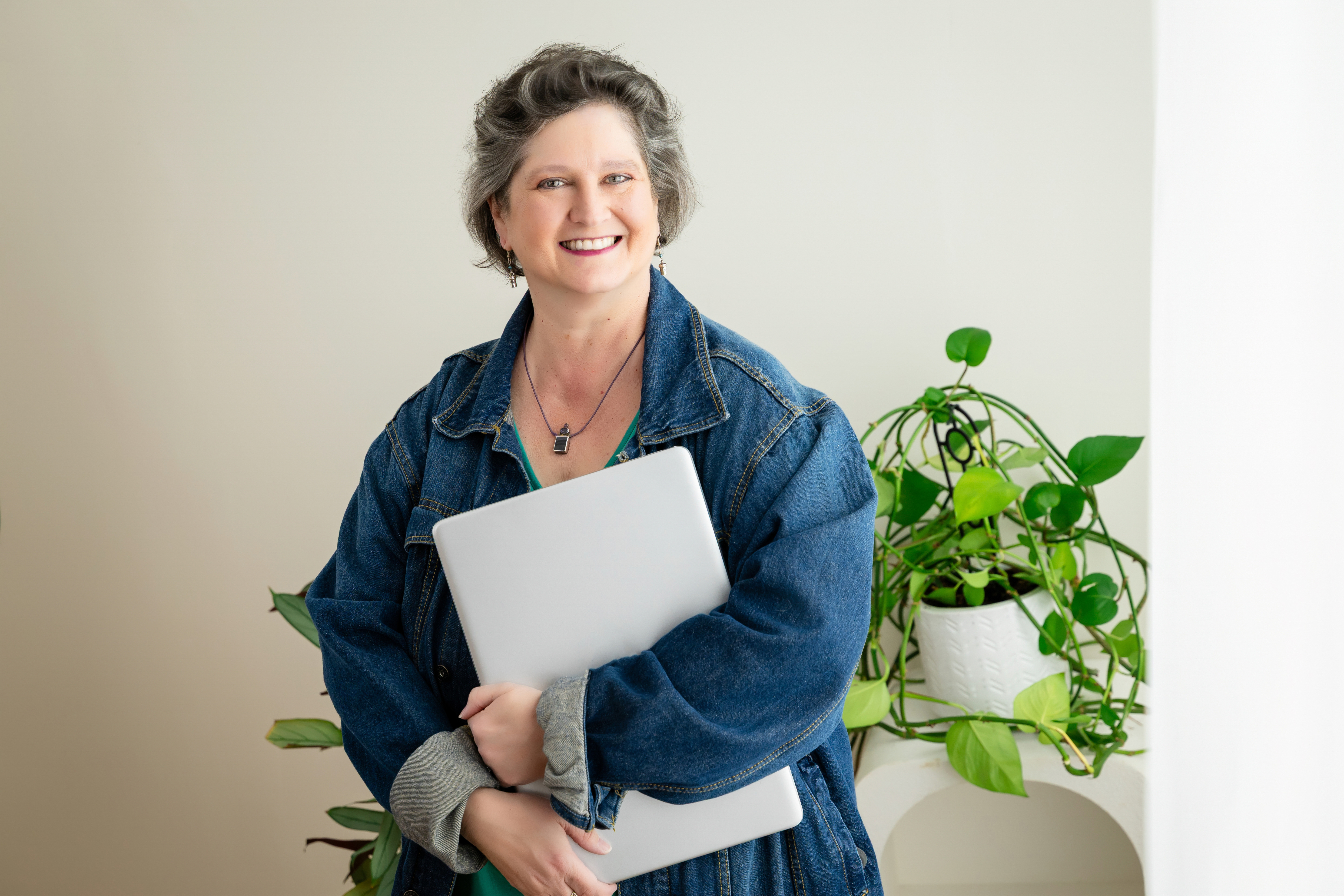 woman in denim jacket holding laptop