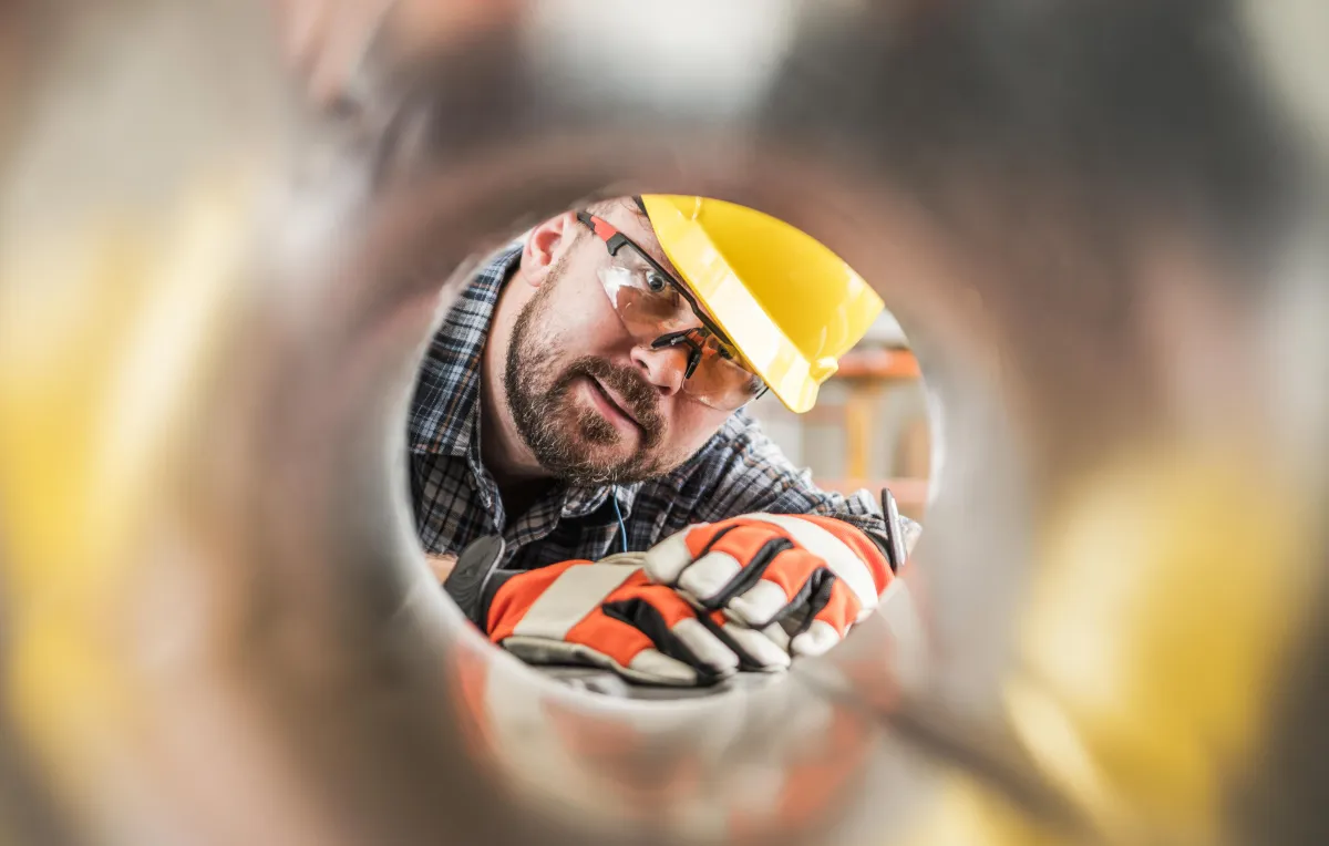 HVAC worker peering through pipe
