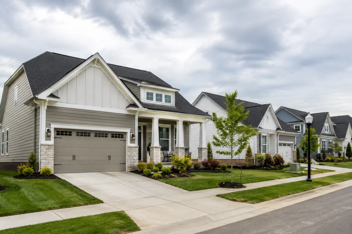 Wider neighborhood perspective of a newer production home in Greenville on a cloudy afternoon, featuring simple landscaping, neighboring homes, clean sidewalks, and a calm residential setting that reflects the mental overload buyers sometimes feel when faced with countless new construction design decisions.