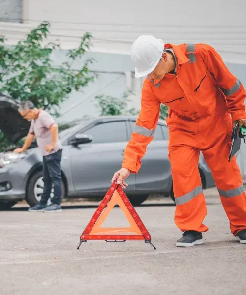 Trusted Roadside Assistance and Towing Service Roadside technician placing warning triangle near broken car while providing professional towing assistance