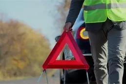 Emergency Roadside Assistance During Vehicle Breakdown Driver placing red warning triangle behind broken down car during emergency roadside assistance situation