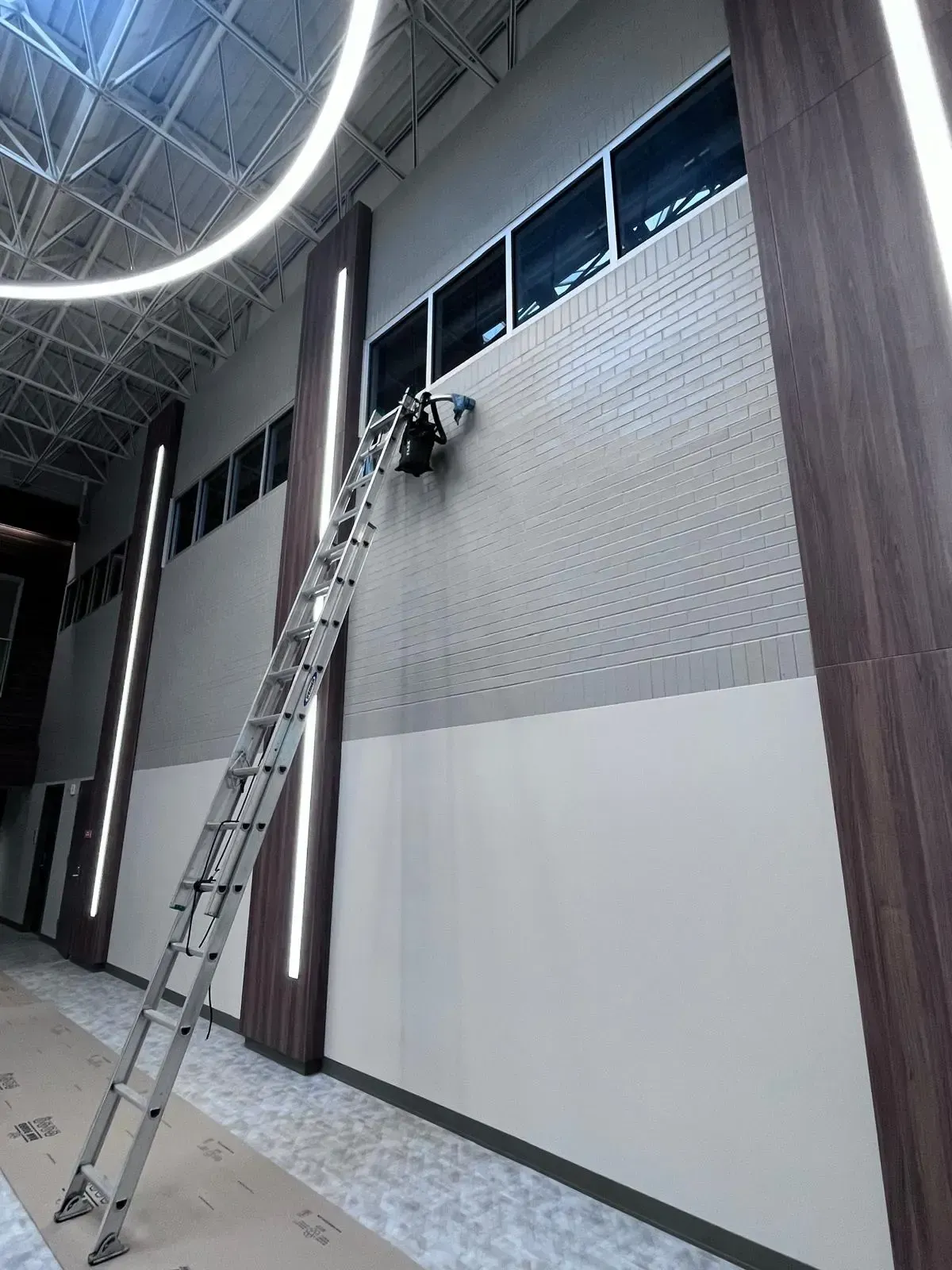 Professional window cleaning technician on ladder installing protective window coverings during commercial building cleaning service in Oklahoma City