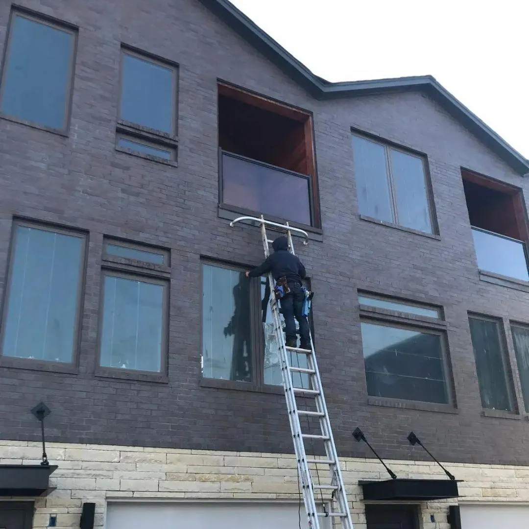 Oklahoma City window cleaning technician safely cleaning multi-story home windows with professional ladder equipmen