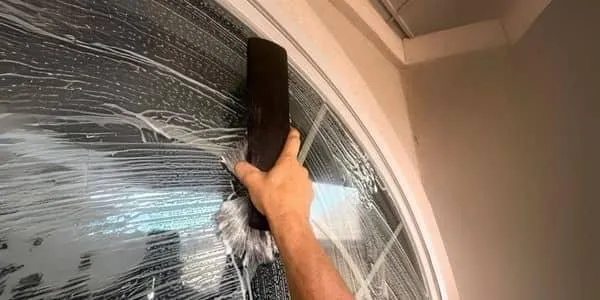 Professional window cleaner in safety harness and hard hat using pressure washing equipment on high-rise building - SudsMonkey Window Cleaning Oklahoma City services