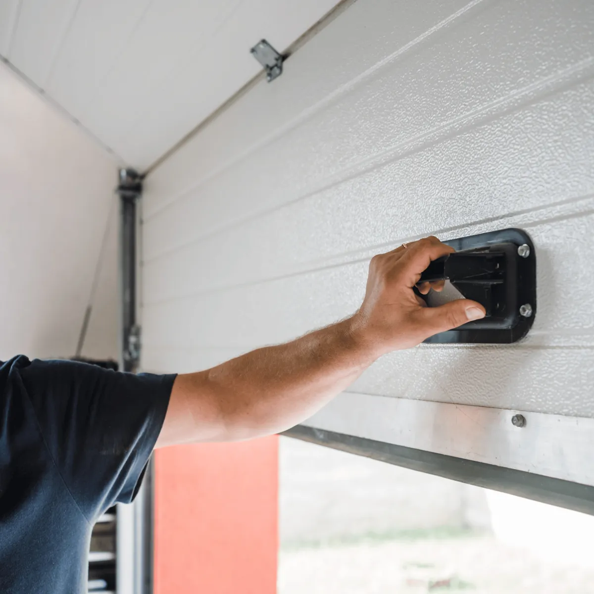 Close-up of a technician’s arm lifting a residential garage door, showing a manual handle and part of the home exterior.