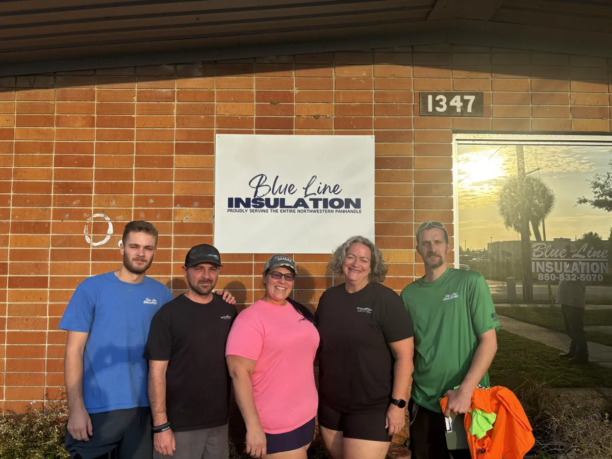 Team photo of Blue Line Insulation in front of their office sign, showcasing their family-owned insulation experts specializing in spray foam, fiberglass batts, blown-in insulation, and insulation removal in the Northwestern Panhandle