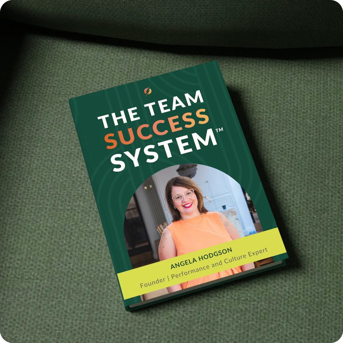 A mock-up of the hook book. The cover contains the title 'The Team Success System', a picture of Angela in a long orange dress, followed by the sub-title 'Angela Hodgson, founder, performance and culture expert'
