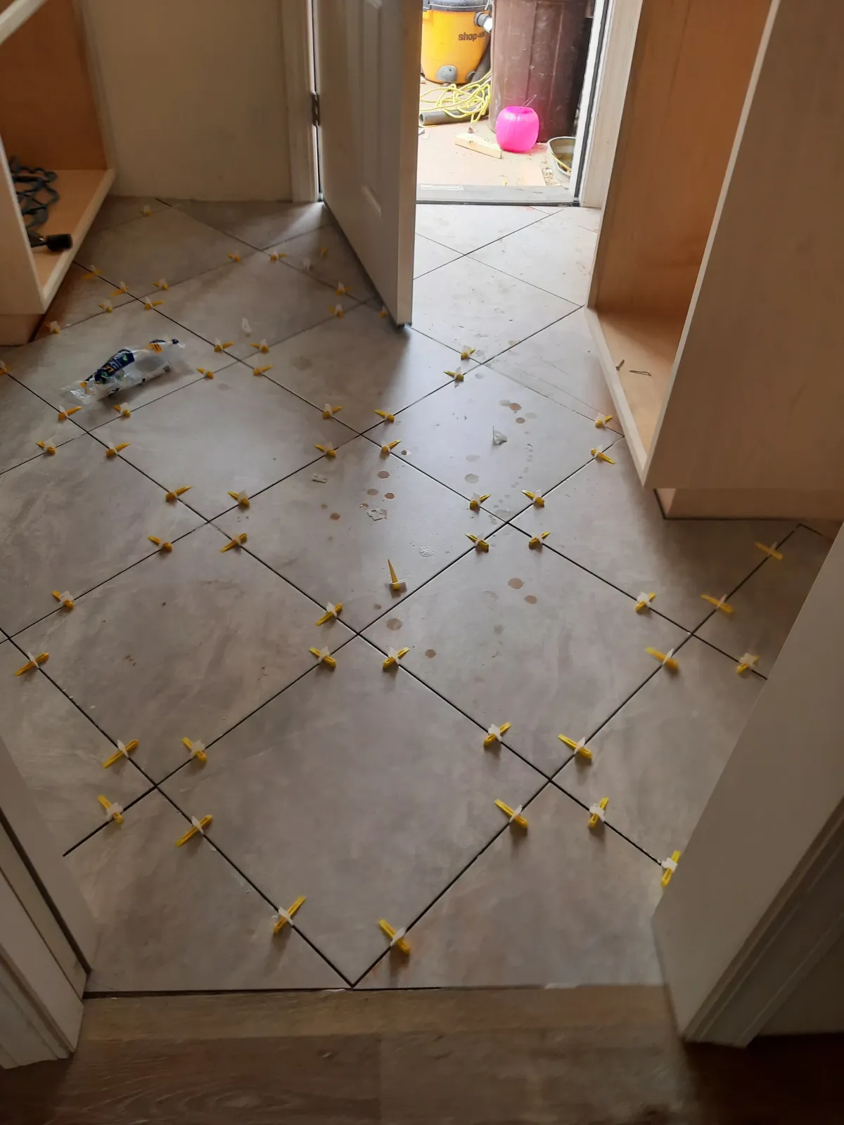 Tile flooring installation in progress, featuring spacers for even grout lines, with an open doorway leading to an outdoor area, showcasing Parker Built Construction's flooring expertise.