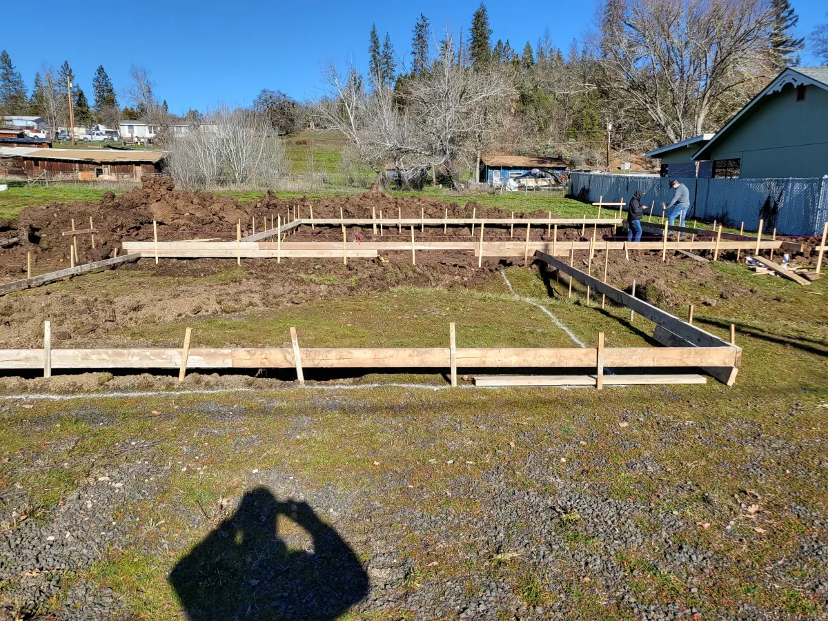 Construction site with excavator preparing foundation for new property build, featuring wooden framing and earthworks in progress.