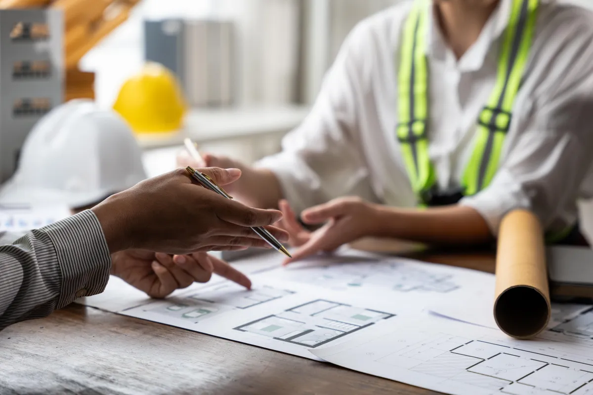 Woman shaking hands with construction worker in safety gear, discussing fencing project details in a partially built indoor space.