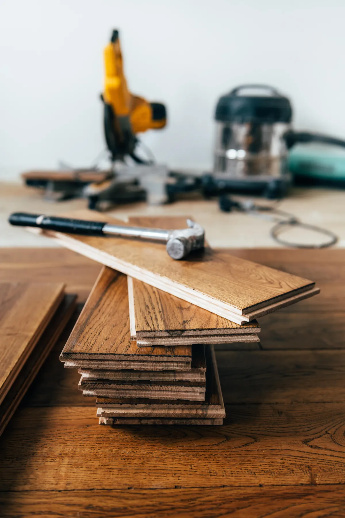 Stack of hardwood flooring planks with a hammer on top and flooring tools in the background, representing professional flooring installation work.