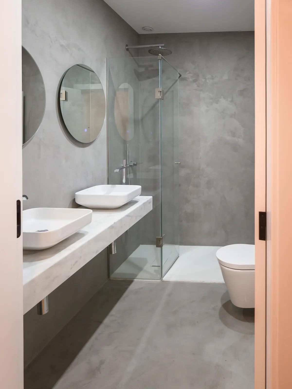Modern bathroom design with floating vanity, double vessel sinks, glass walk-in shower, and minimalist gray tile finishes.