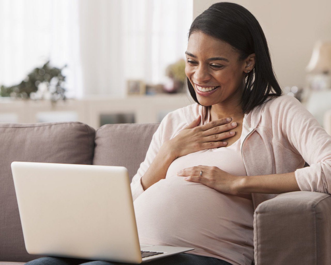 A pregnant woman smiling at her laptop