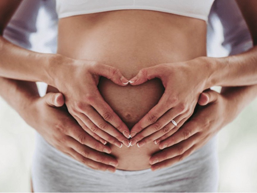Hands making a heart shape on a pregnant belly