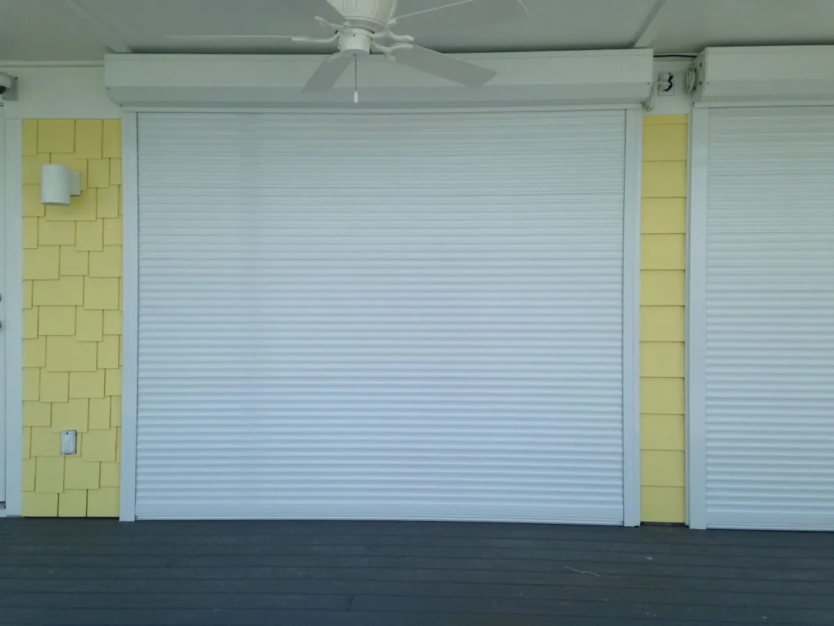 White roll-down hurricane shutter closed over a patio opening on a yellow home in Panama City Beach, FL
