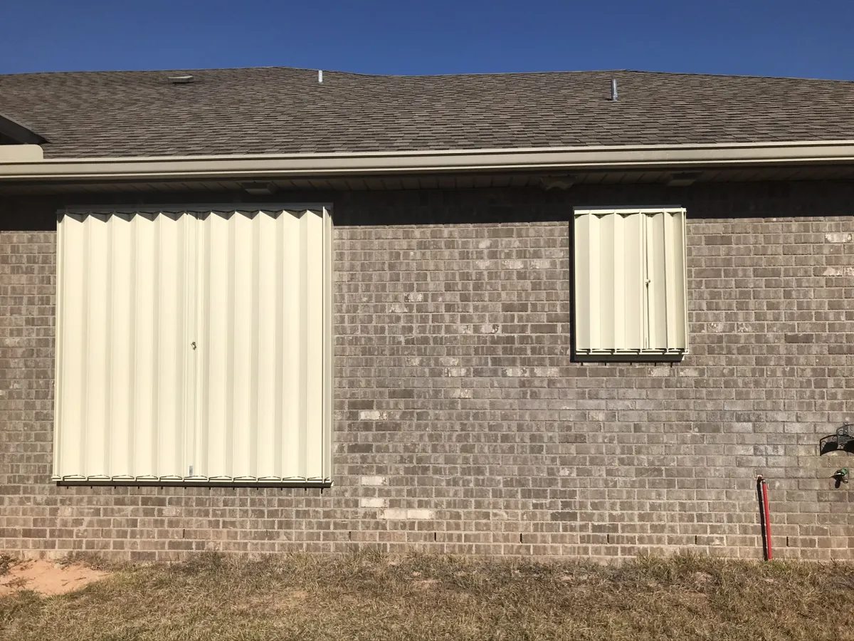 Cream accordion hurricane shutters mounted on a brick home in Pensacola, FL