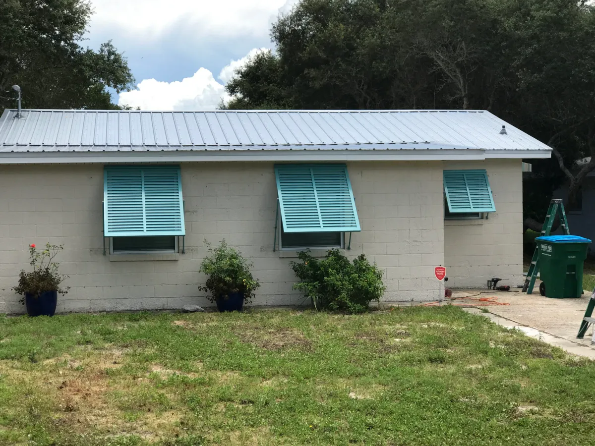 Teal Bahama shutters over windows on a single-story home with a metal roof in Gulf Breeze, FL