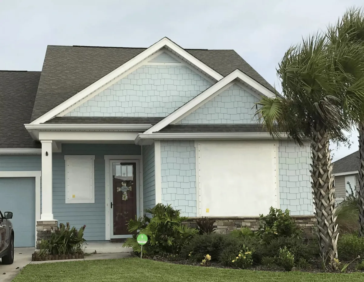 Light blue home with white storm panels covering the windows before a hurricane in Panama City Beach, FL