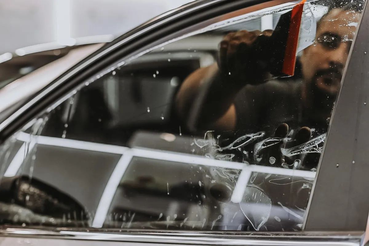 Silhouette of a masked person in a hood and gloves prying open a car window with a flashlight
