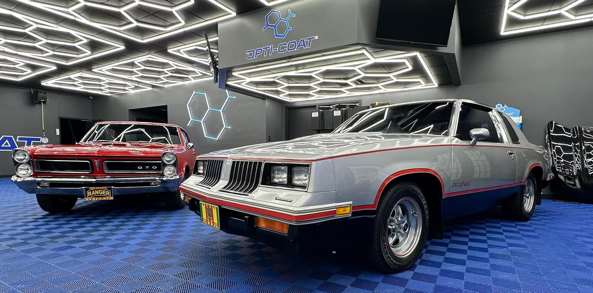 White sports coupe parked on concrete in front of a light-colored building, shown in a front three‑quarter view