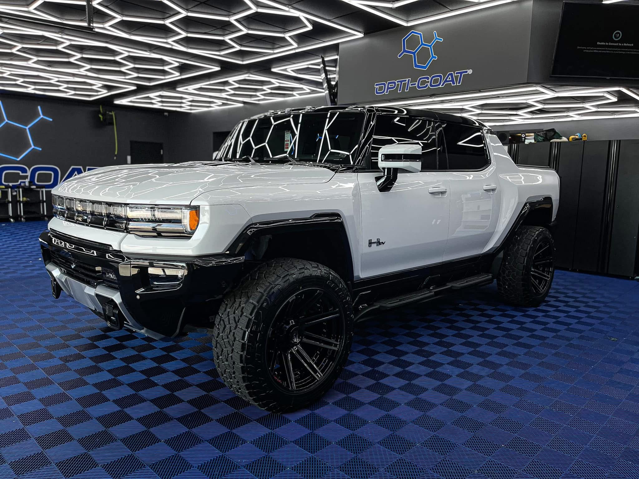 White sports coupe parked on concrete in front of a light-colored building, shown in a front three‑quarter view