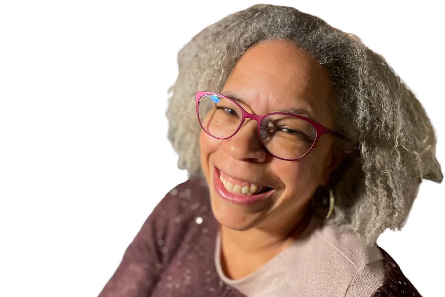 anya Spencer smiling warmly with silver curls and pink glasses, wearing a sparkly top against a bold purple background. Embodies confident, approachable leadership for women ready to communicate with power.