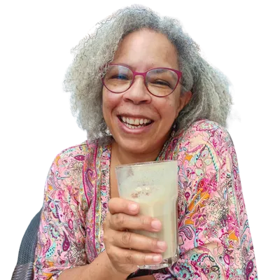 Tanya Spencer smiling warmly while holding a chai latte, wearing a colorful patterned top against a deep purple background. Captures her friendly, grounded presence as a leadership communication coach for women