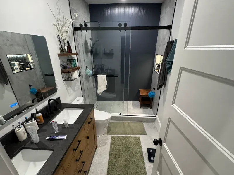 Full bathroom remodel with large-format porcelain floor tile, frameless sliding glass shower enclosure, and dark granite vanity by CLA New England Tile – Boston MA