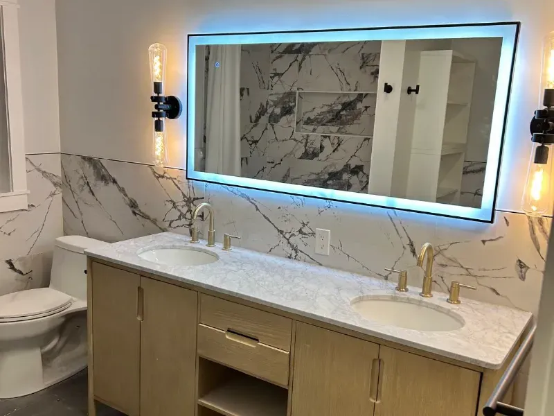 Double vanity bathroom with large-format marble tile backsplash, LED backlit mirror, and gold faucets installed by CLA New England Tile – Greater Boston Area