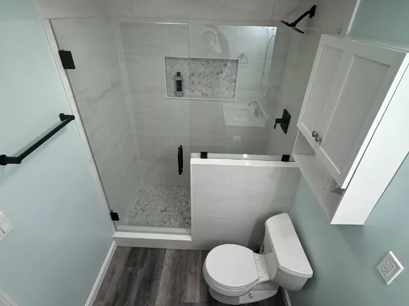 Small bathroom remodel with white subway tile shower, mosaic tile floor, frameless glass enclosure and hardwood flooring by CLA New England Tile – Massachusetts