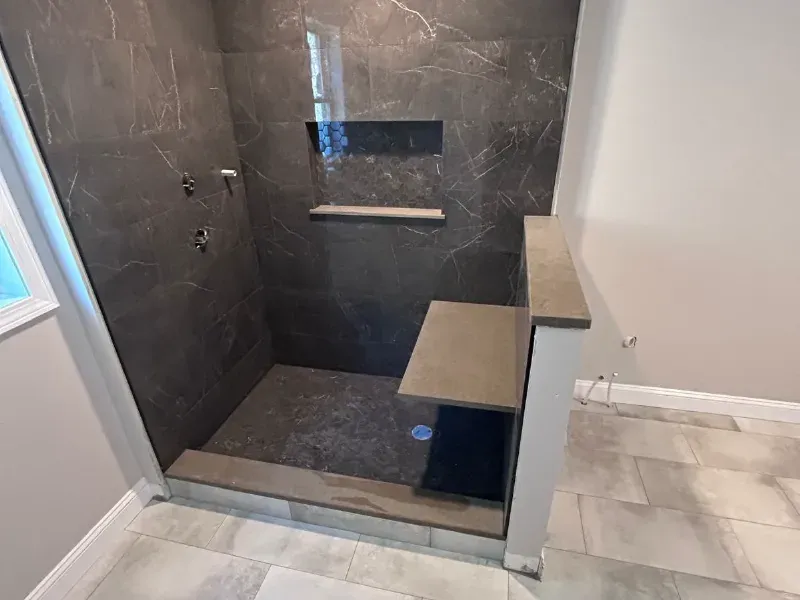 Walk-in shower with large-format dark marble porcelain tile, built-in bench, recessed niche, and hexagon accent tile installed by CLA New England Tile – Greater Boston