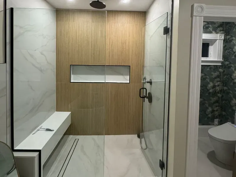 Frameless glass shower with wood-look porcelain accent wall, Calacatta marble floor tile, built-in bench and niche by CLA New England Tile – Greater Boston