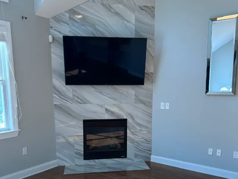 Floor-to-ceiling large-format marble porcelain tile fireplace accent wall with TV mount area in residential living room by CLA New England Tile – Boston MA